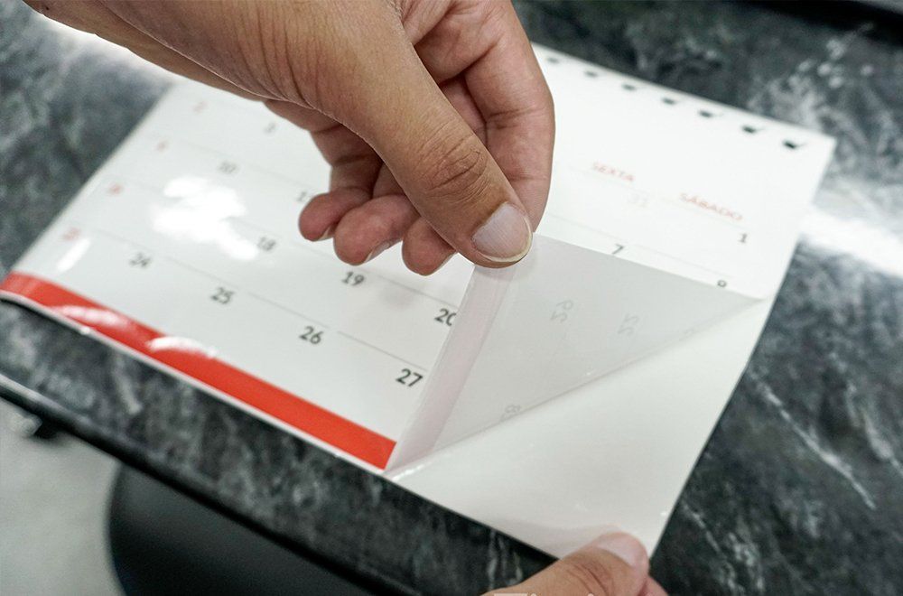 Mãos descolando o canto de uma página branca de um calendário de mesa com datas impressas.