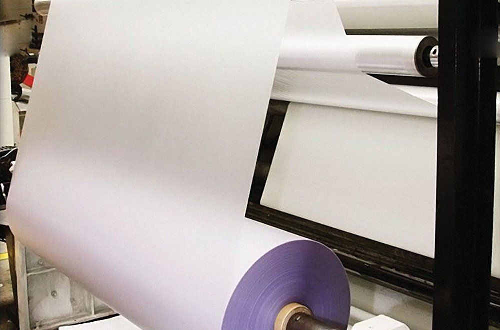 Um rolo de material branco desenrolando-se em uma máquina em um ambiente industrial ou de manufatura.