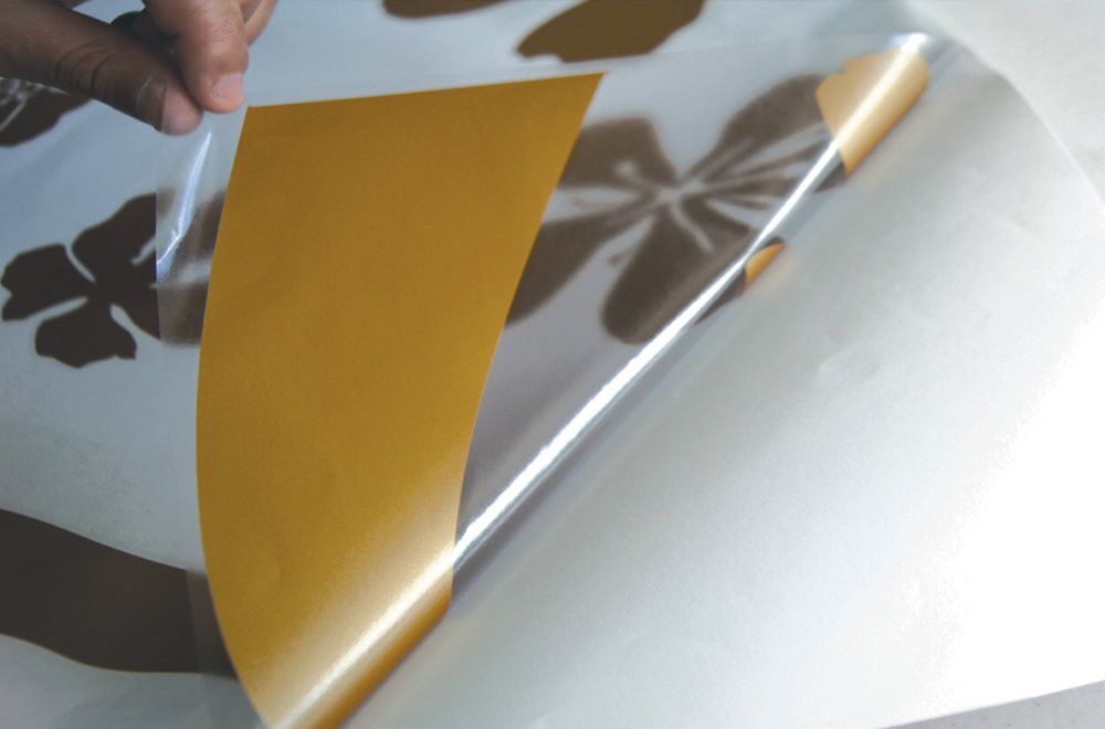 Uma mão retira um decalque adesivo marrom com estampa floral de seu suporte de papel branco.