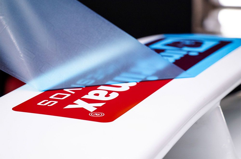 Uma película protetora azul está sendo removida de uma superfície branca, revelando por baixo o logotipo vermelho e azul