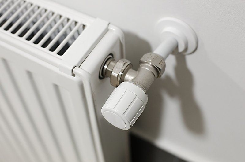 Primo piano di un radiatore bianco con una manopola della valvola termostatica a parete.