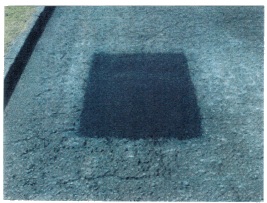 Dark square patch on cracked asphalt.