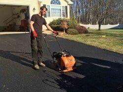 Man compacting asphalt driveway with plate compactor.