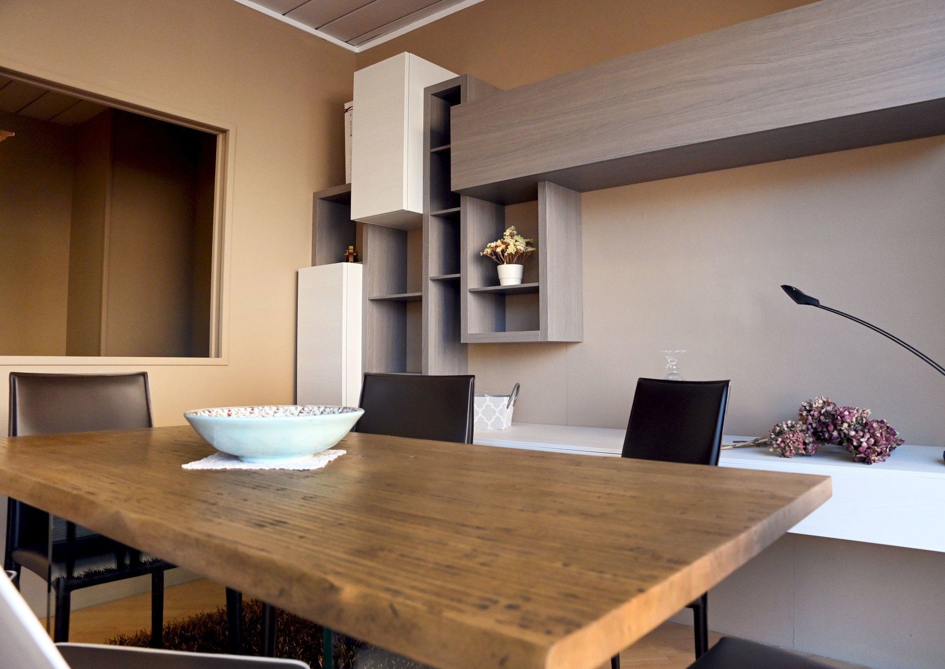 Sala da pranzo moderna con tavolo in legno, sedie nere e mensole a muro integrate.