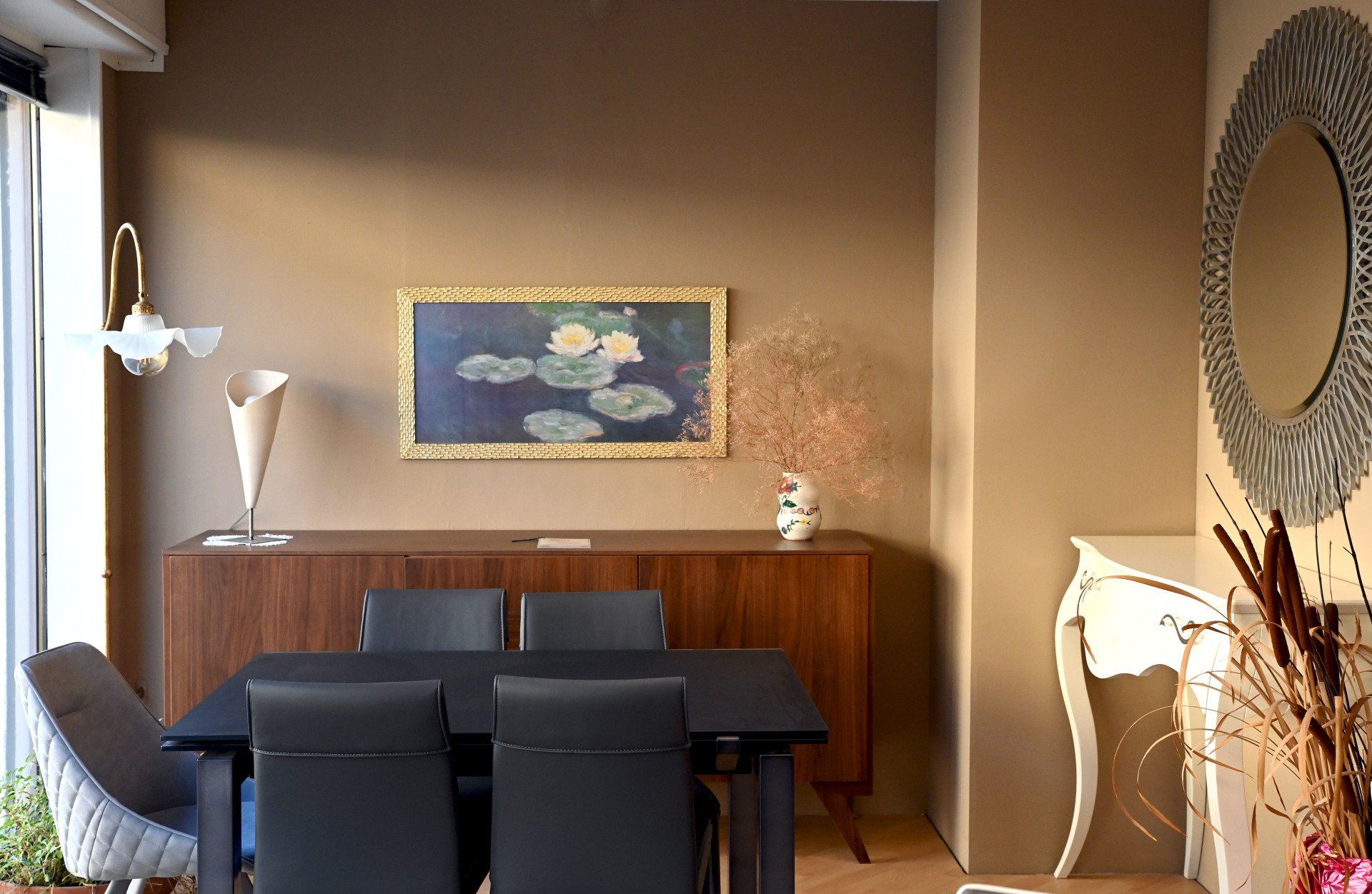Sala da pranzo moderna con tavolo, sedie, credenza scuri e quadri incorniciati alle pareti in calde tonalità beige.