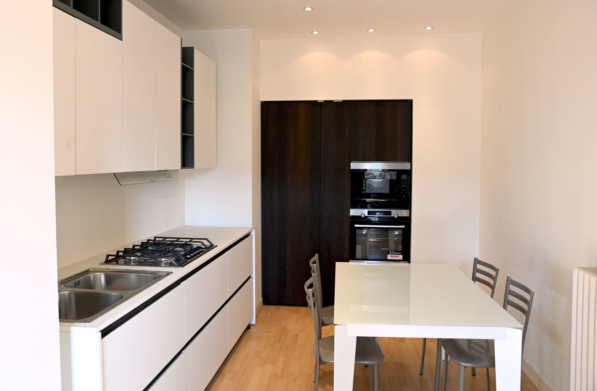 Cucina moderna bianca con piano cottura a gas, lavello, tavolo da pranzo e mobili in legno scuro.