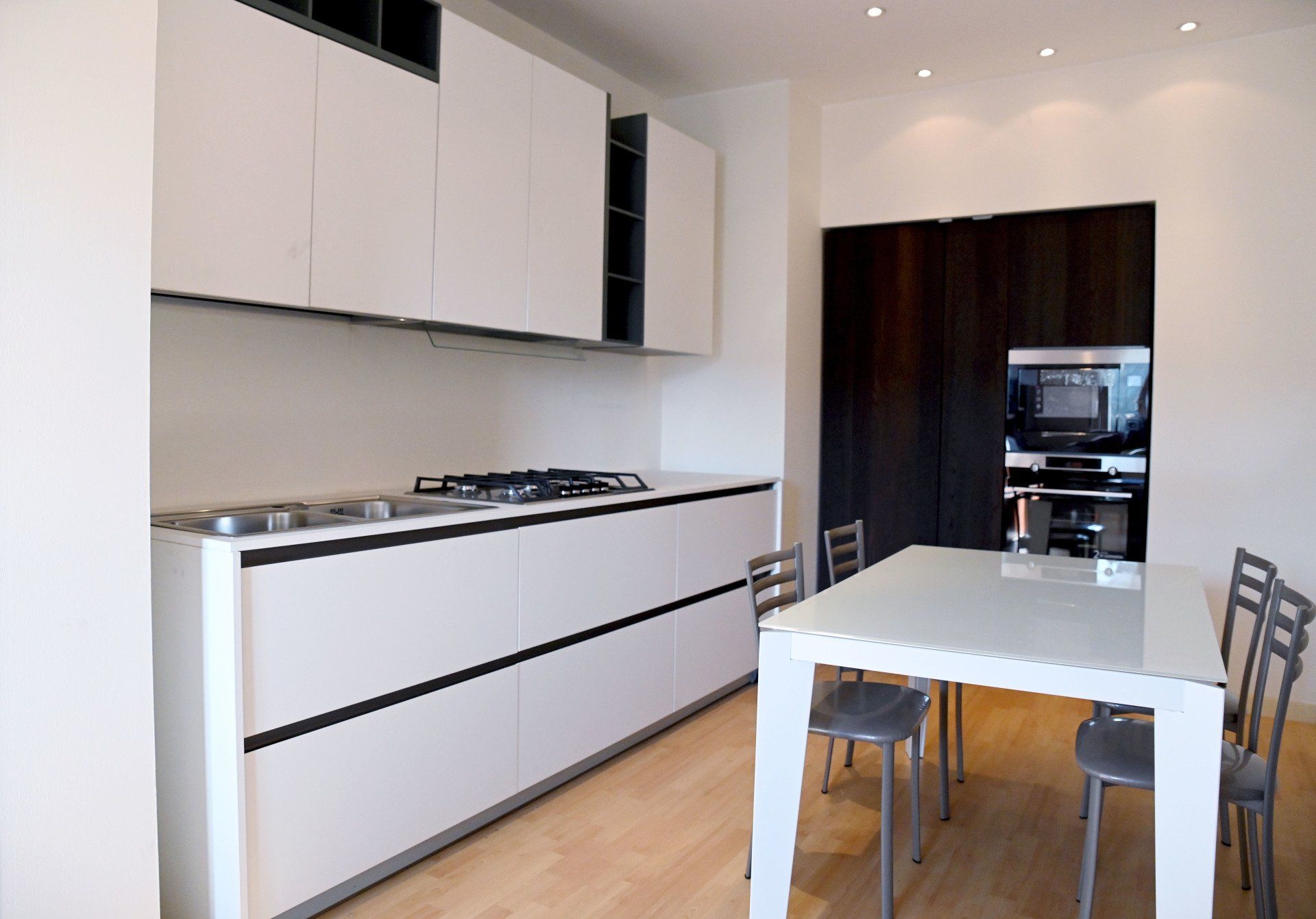 Cucina-sala da pranzo moderna con mobili bianchi, tavolo da pranzo e sedie in una stanza luminosa