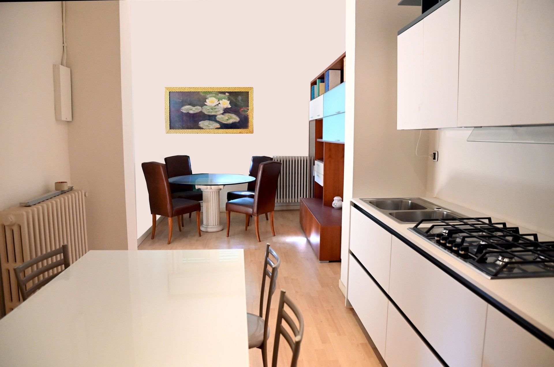 Cucina e zona pranzo moderne con mobili bianchi, pavimento in legno e un tavolo vicino alla finestra.
