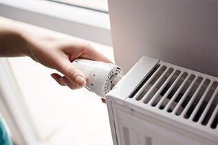 Hand Adjusting Thermostat - Plumbing Repair in Yorkville, IL A person adjusting the dial of a white radiator. The dial is being turned with a hand near a window.