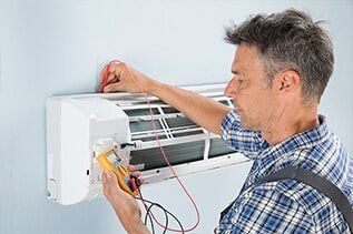 Technician Testing Air Conditioner - Plumbing Repair in Yorkville, IL An electrician tests an indoor air conditioner unit with a multimeter. He's wearing a plaid shirt and is focused on his work.