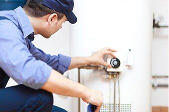 Water Heater Repair - Plumbing Repair in Yorkville, IL A plumber adjusting a dial on a white water heater in a utility room, wearing a blue uniform and cap.