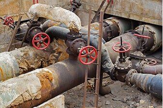 Drain Line Repair - Plumbing Repair in Yorkville, IL Rusty industrial pipes with red valves, possibly in an outdoor setting. Brown and white insulation is peeling off the pipes.