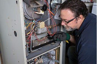 Furnace Repair - Plumbing Repair in Yorkville, IL A man with glasses and gloves works on a furnace, inspecting wiring and components inside the open unit.