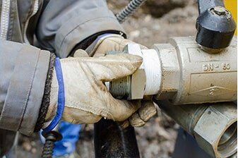 Sewer Repair - Plumbing Repair in Yorkville, IL A worker wearing gloves tightly screws a metal fitting onto a pipe, applying white sealant tape.