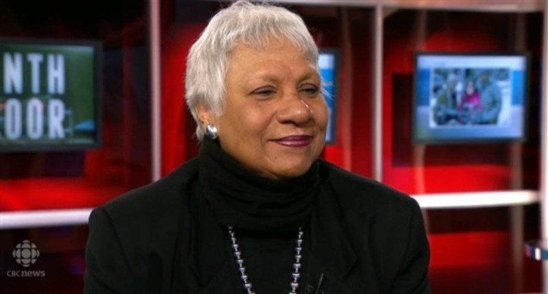 A woman in a black turtleneck is sitting in front of a sign that says nth door.