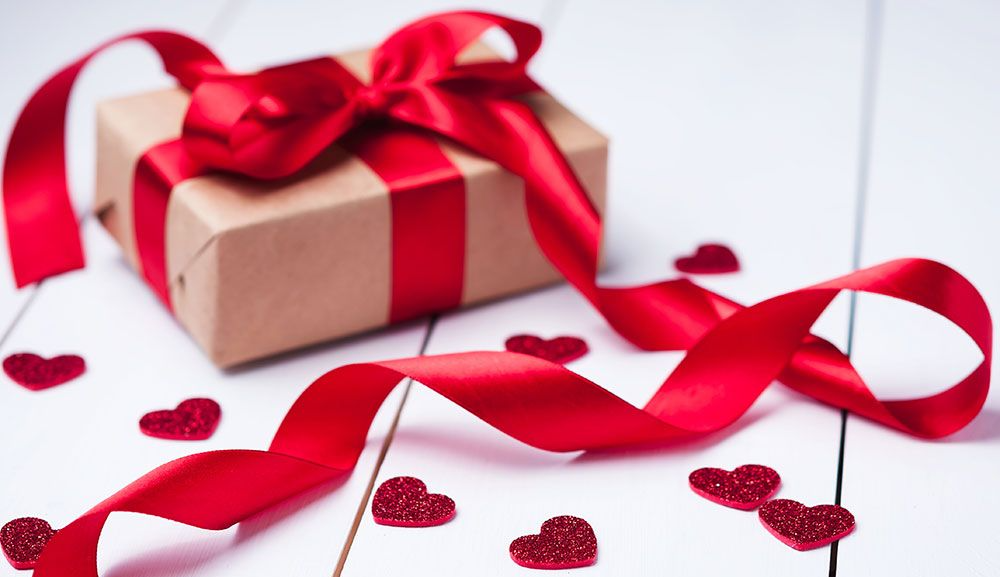 A gift box with a red ribbon and bow is surrounded by red hearts.