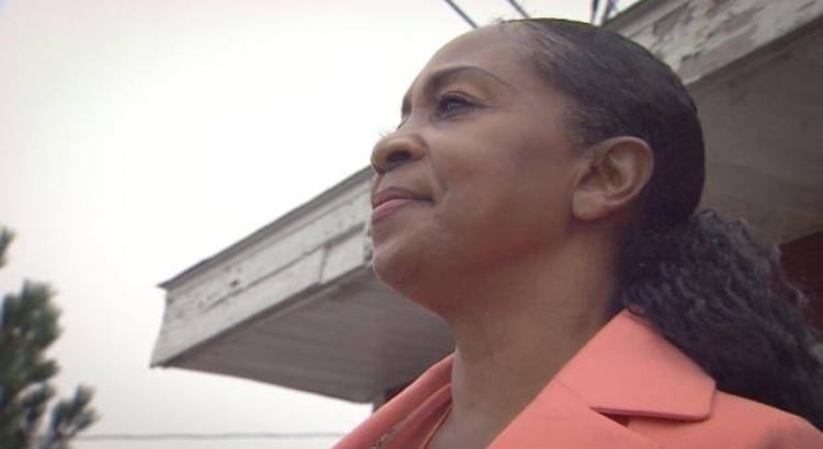 A woman in a pink jacket is standing in front of a building.