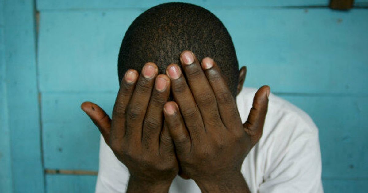 Black Canadians and HIV A man is covering his face with his hands in front of a blue wall.