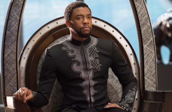 A man in a black suit is sitting on a throne.
