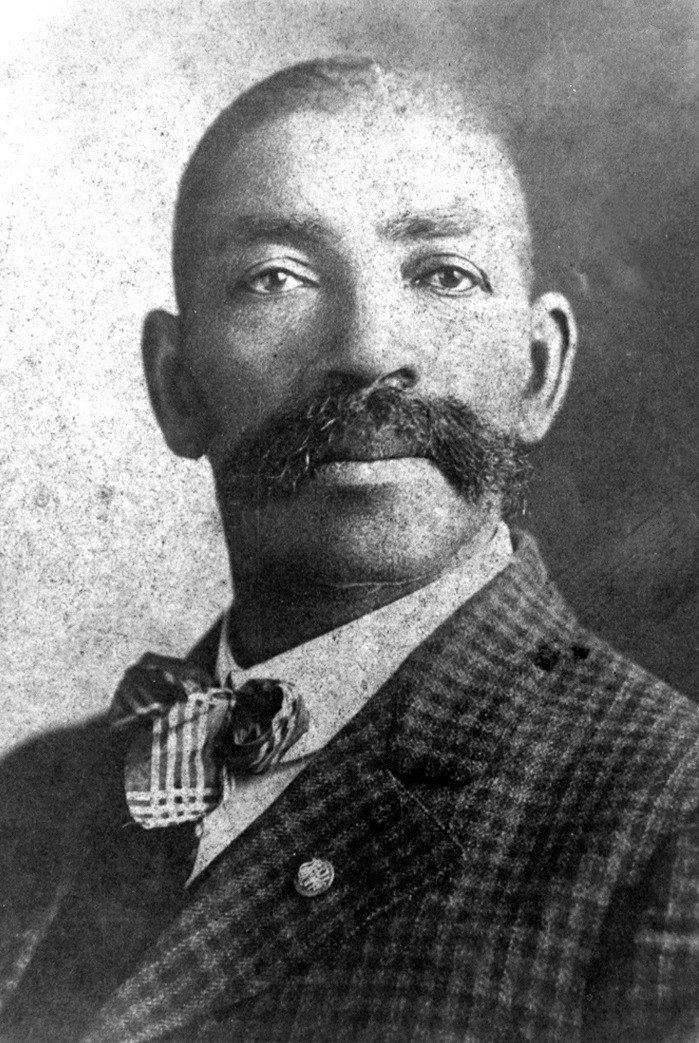 A black and white photo of a man with a mustache wearing a suit and bow tie.