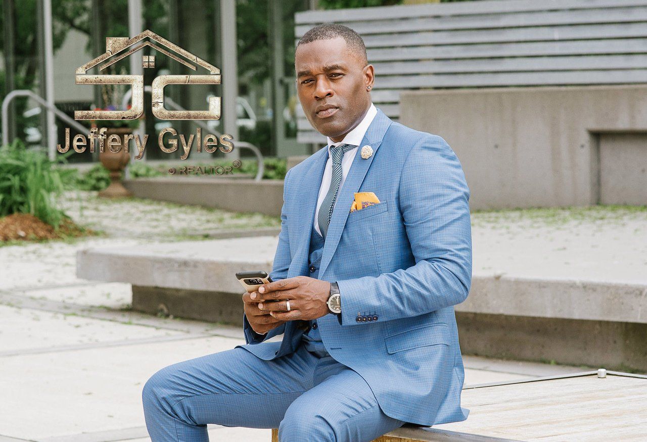 A man in a blue suit and tie is sitting on a bench looking at his phone.