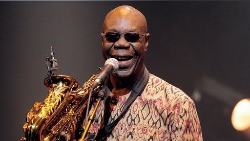 A bald man is playing a saxophone and singing into a microphone.