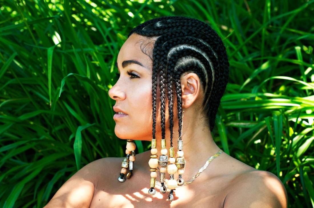 A woman with braids and earrings is standing in the grass.