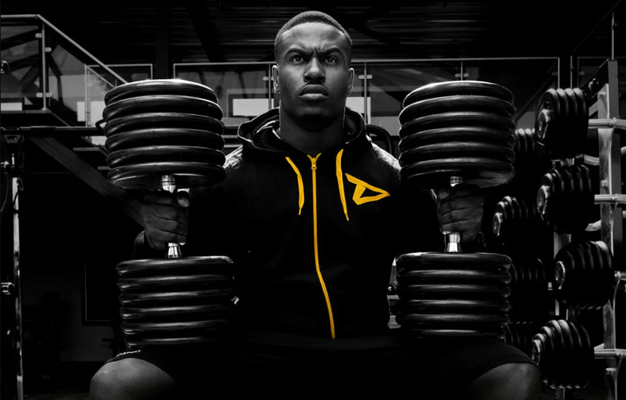 A man is sitting in front of a stack of dumbbells in a gym.