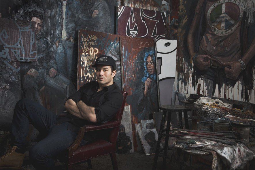 A man is sitting in a chair in front of a wall with graffiti on it.