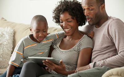 A family is sitting on a couch looking at a tablet.