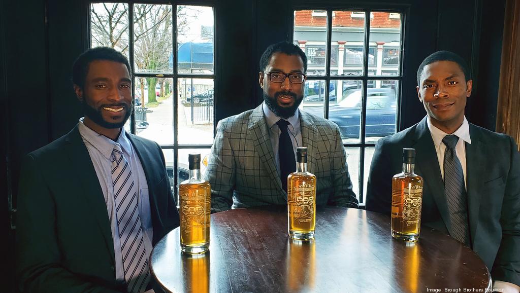 Three men in suits and ties are sitting at a table with bottles of alcohol.
