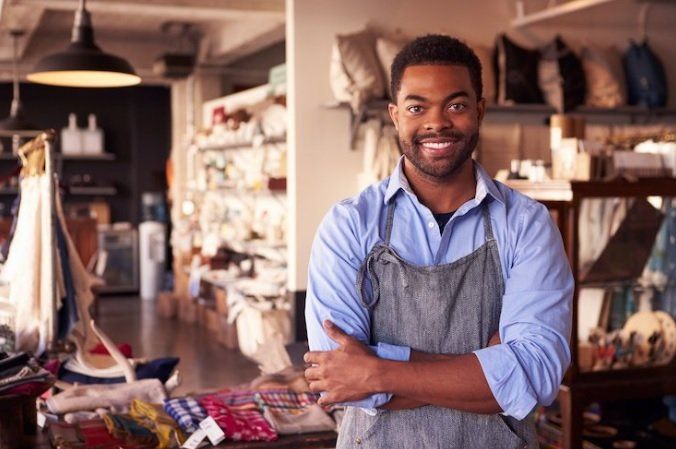 A man in an apron is standing in a store with his arms crossed.
