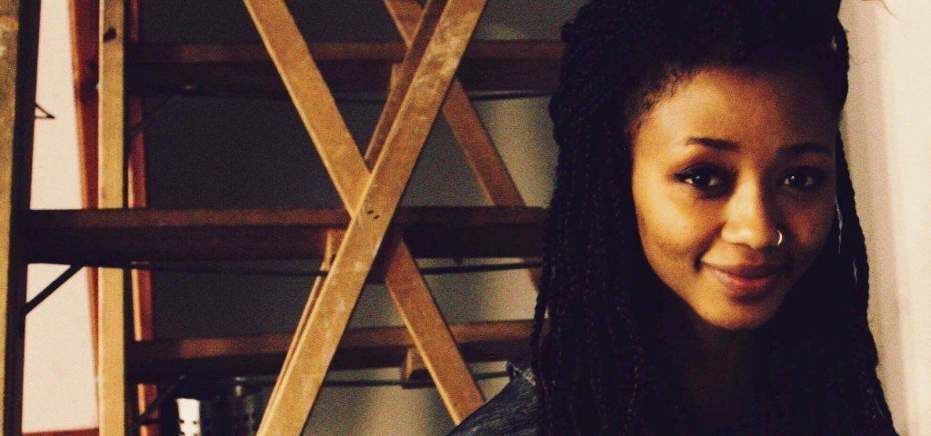 A woman with dreadlocks is standing in front of a wooden shelf.