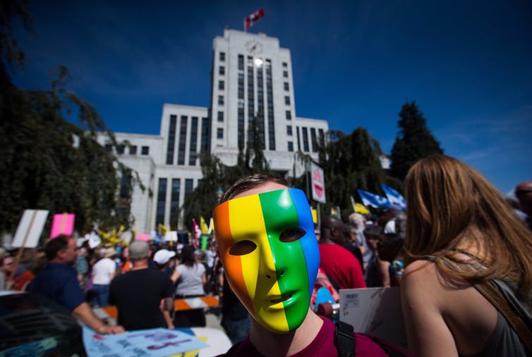 A man wearing a rainbow mask participates in an anti racist protest