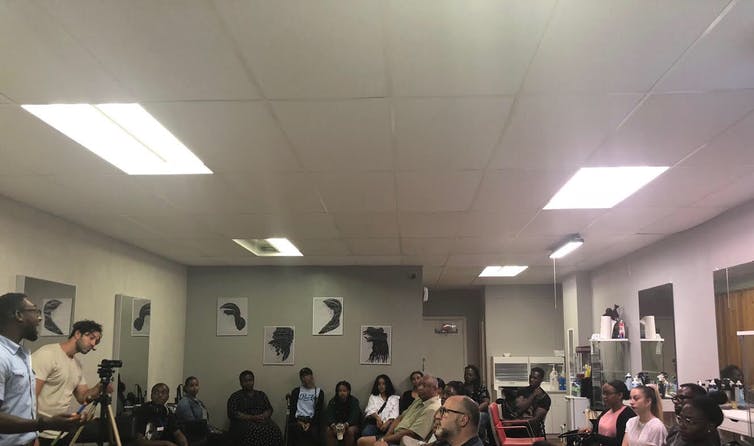 A group of people are sitting in a room in a barber shop.