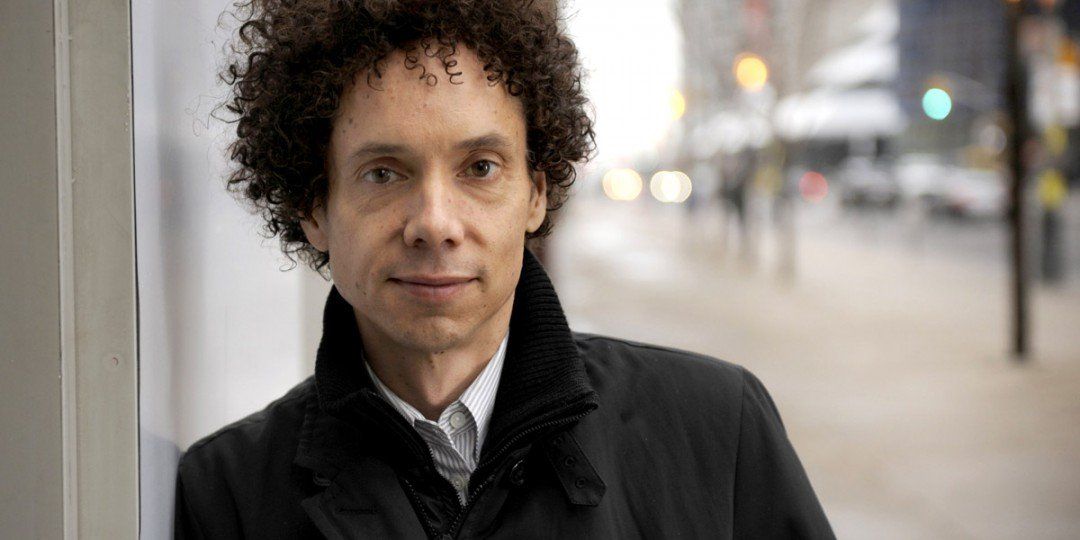 A man with curly hair is leaning against a wall.