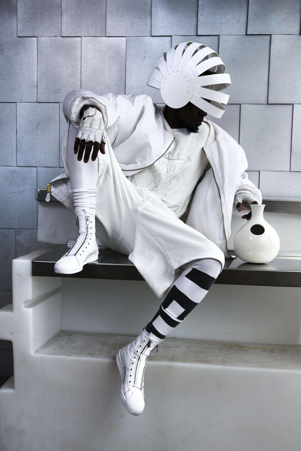 A person in a white costume is sitting on a ledge holding a vase.