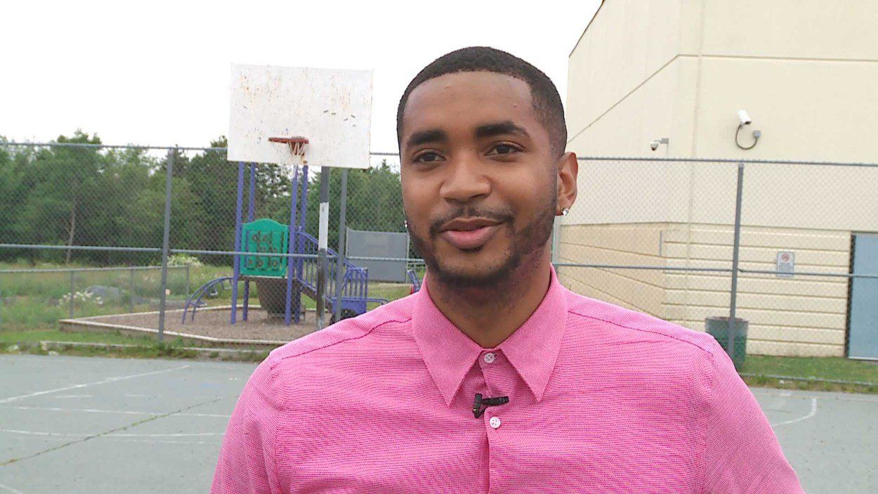 A man in a pink shirt is standing in front of a basketball court.