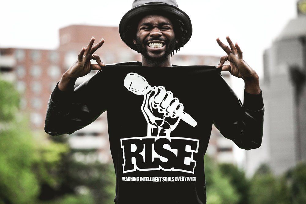 A man wearing a black shirt that says rise is holding a microphone.