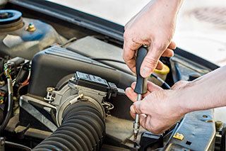 A man is working on the engine of a car with a screwdriver.