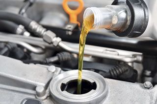 A close up of a person pouring oil into a car engine.