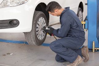 A man is changing a tire on a white car in a garage.