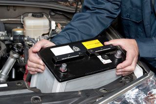 A man is holding a car battery under the hood of a car.