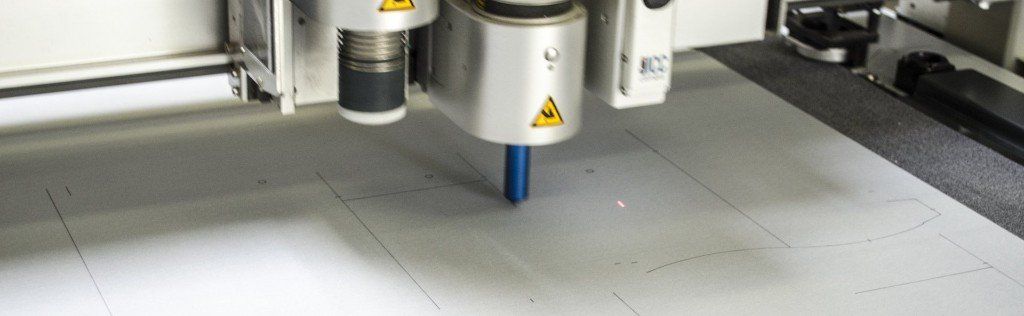 Een machine die een wit materiaal snijdt. De machine heeft een blauwe snijpunt.