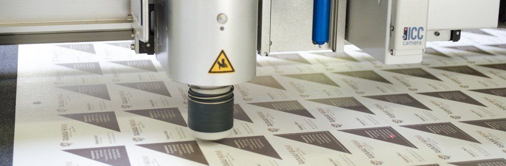 Een machine die geprinte vormen uit een vel papier snijdt. De machinekop is voorzien van een laserwaarschuwingssymbool.