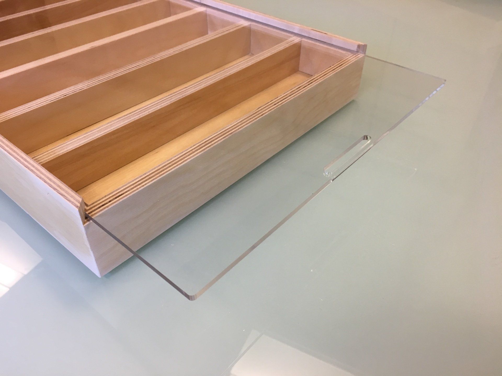 Houten doos met tussenschotten en een transparant schuifdeksel op een glanzend oppervlak.