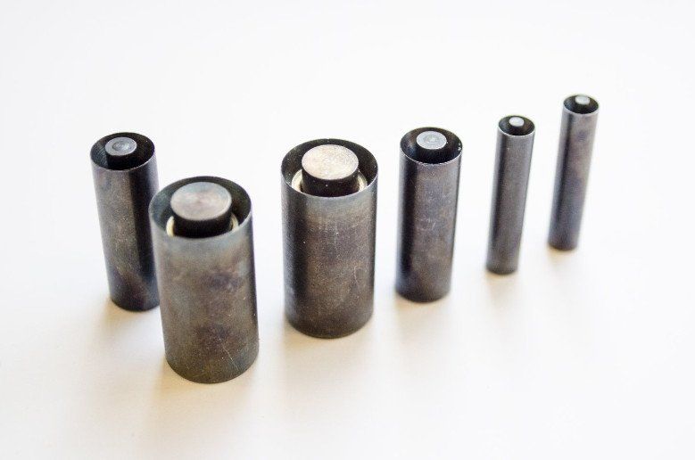 Zes cilindrische metalen ponsen van verschillende afmetingen, gerangschikt op een wit oppervlak.