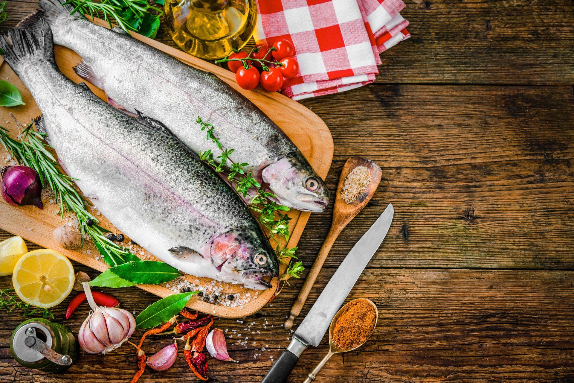 Dos peces están sentados sobre una tabla de cortar de madera rodeados de verduras y especias.