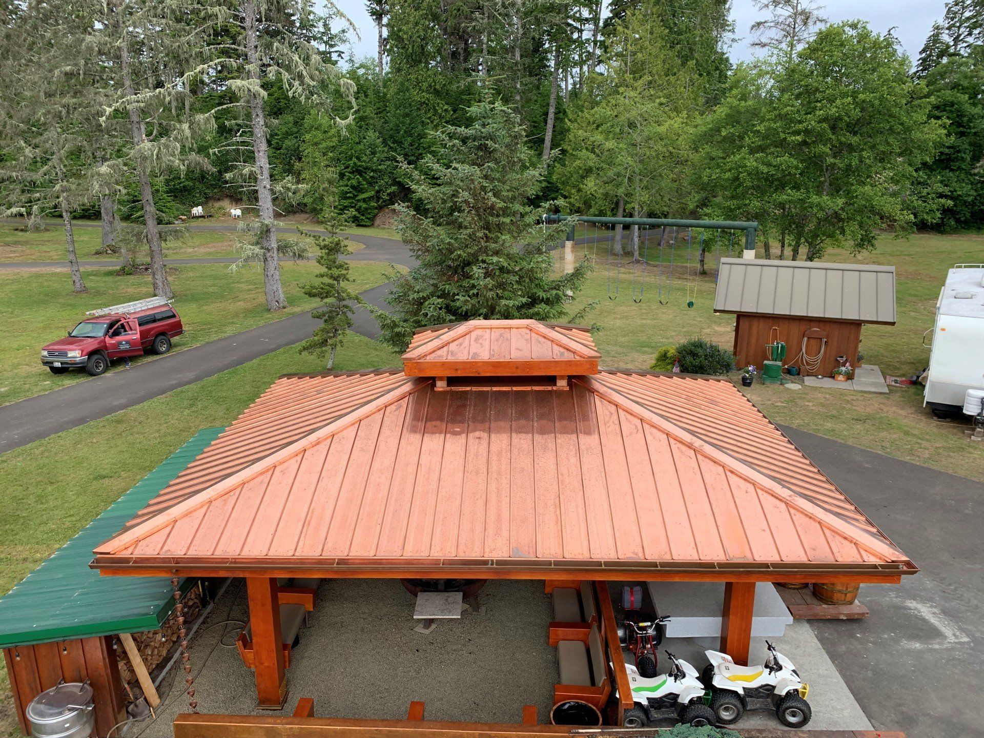 Orange-roofed shelter in a park; a red truck on the path, ATVs parked, and a small building are nearby.
