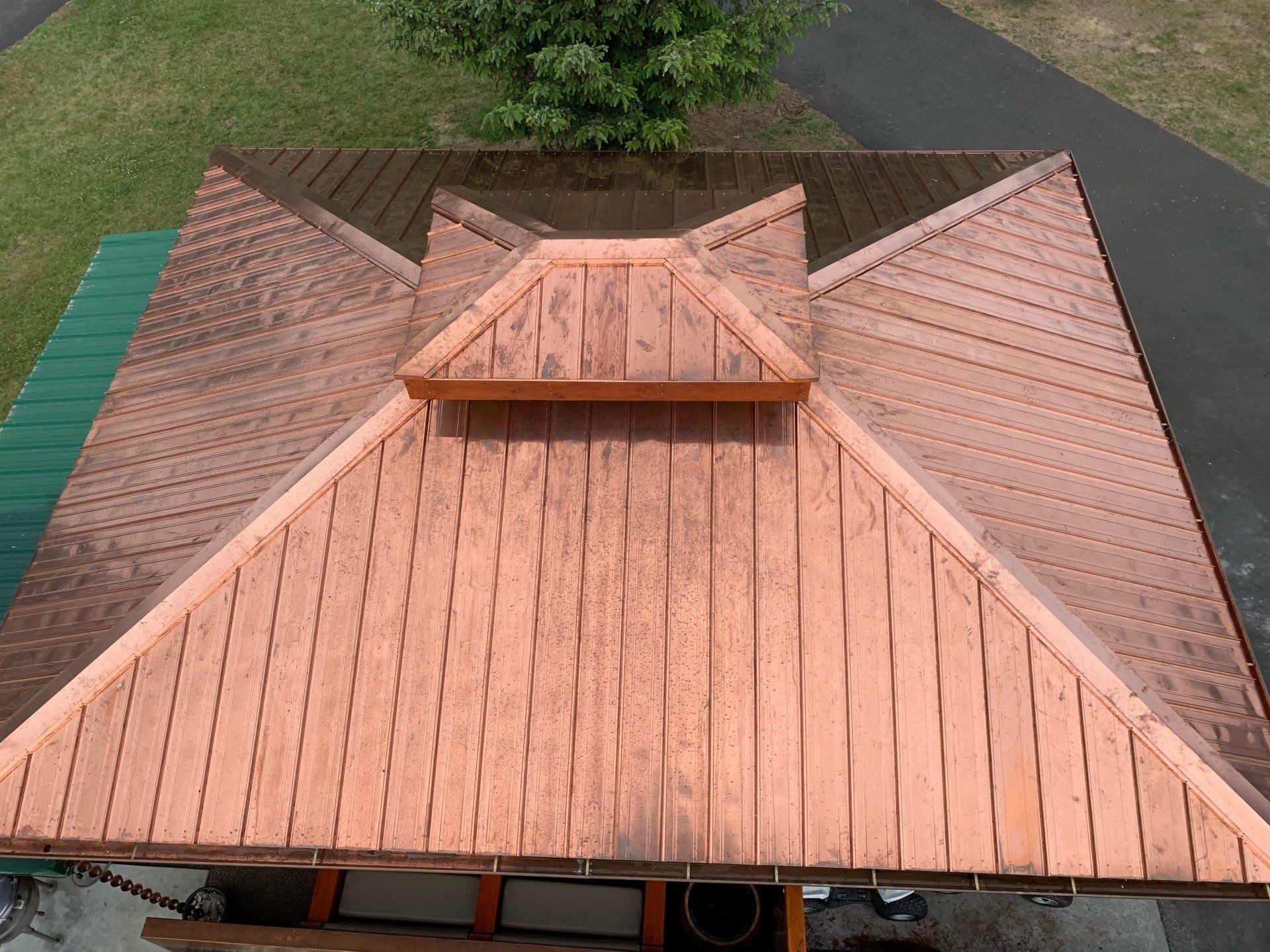 Overhead view of a copper roof with a central raised section and surrounding triangular panels, set outdoors.